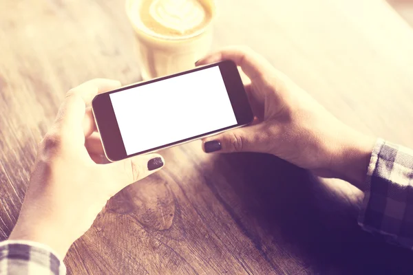 Mãos de menina com smatphone em branco e xícara de café em uma ta de madeira — Fotografia de Stock