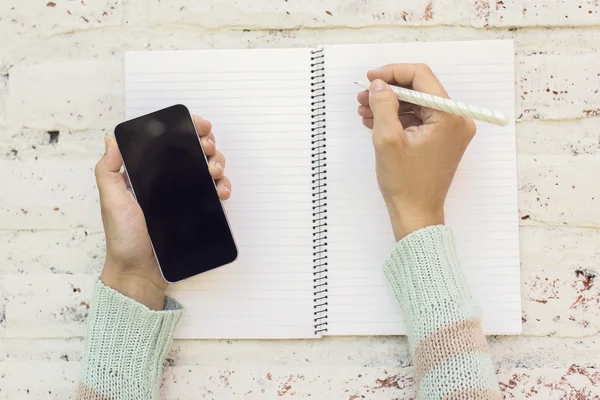 Girl hands with smartphone and blank diary with pen on a wooden — Stock Photo, Image