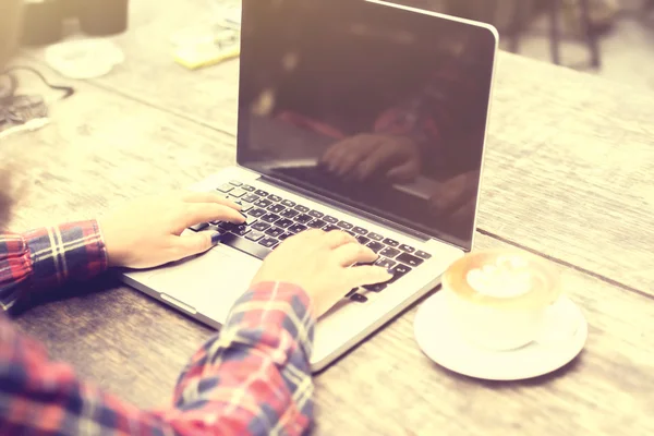 Menina digitando com laptop e cappuccino em uma mesa de madeira — Fotografia de Stock