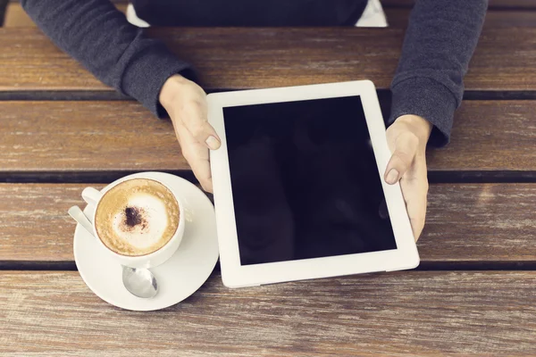 Manos de niña con tableta digital y taza de café en una pestaña de madera —  Fotos de Stock