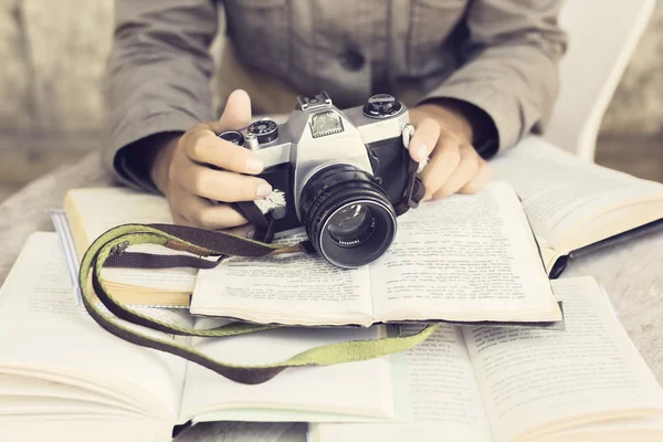 Händer med gamla kamera och flera öppna böcker på ett träbord — Stockfoto