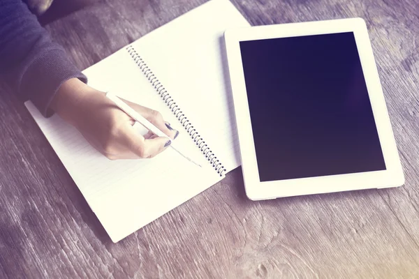 Mädchen schreibt in Notizbuch mit digitalem Tablet — Stockfoto