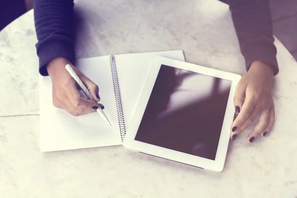 Menina escreve em um caderno e trabalhando com tablet digital — Fotografia de Stock