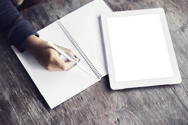 Chica escribe en un cuaderno acostado al lado de una tableta digital en blanco —  Fotos de Stock