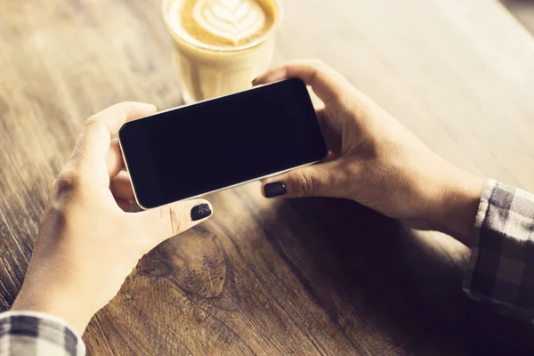 Girl's hands with smartphone and coffee on a wooden table — Stock Photo, Image