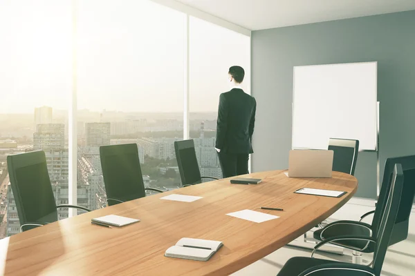 Empresário na moderna sala de conferências com placa em branco e cidade — Fotografia de Stock