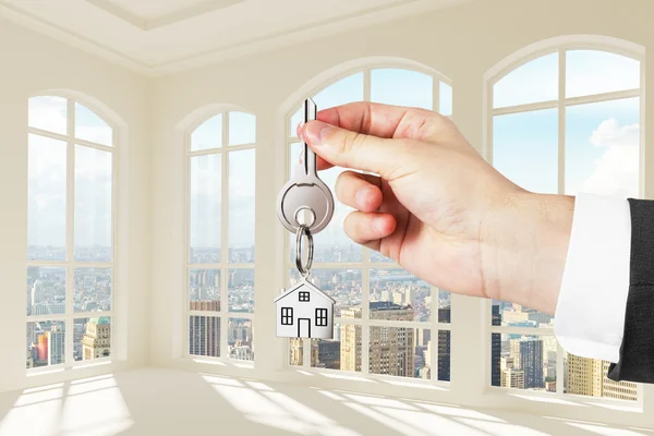 Man with key in hand in modern sunny white room with city view