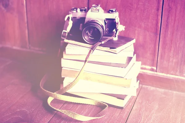 A pile of books and old style photo camera on wooden floor, inst