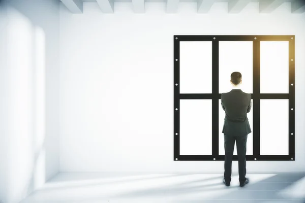 Бизнесмен смотрит в окно в светлой пустой комнате — стоковое фото