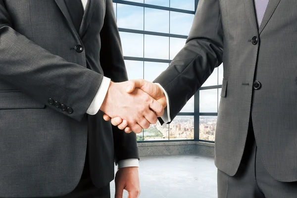 Business partners shake hands in empty loft office — Stock Photo, Image