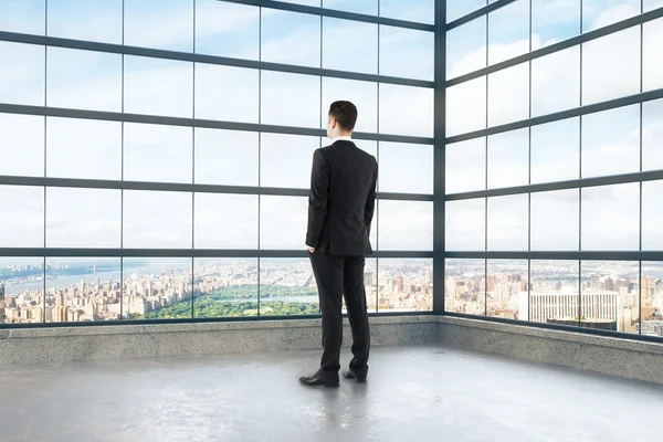 Geschäftsmann schaut aus dem Fenster des leeren Dachgeschosses — Stockfoto