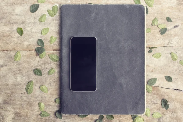 Smartphone preto em branco com caderno de exercícios e folhas em madeira t — Fotografia de Stock