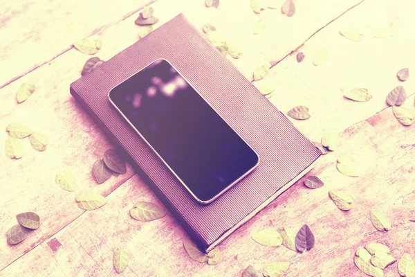 空白的手机屏幕用日记和木制的桌子上的树叶 — 图库照片