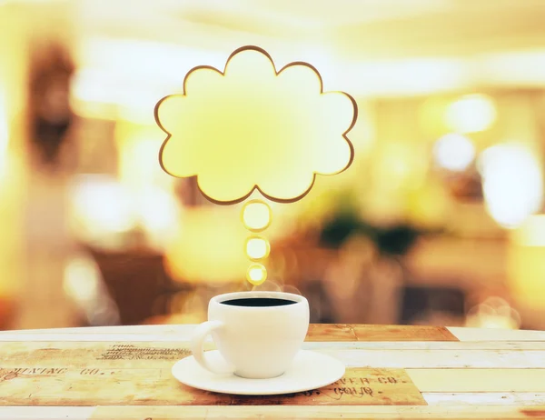 Cup of coffee with yellow speach bubble on wooden table — Stock Photo, Image