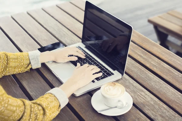 Menina com laptop e xícara de café na mesa de madeira — Fotografia de Stock