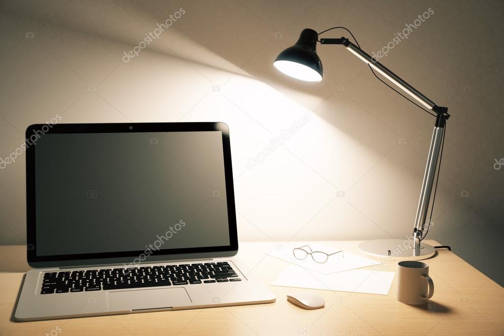 Blank black laptop screen with coffee mug and a lamp on wooden t