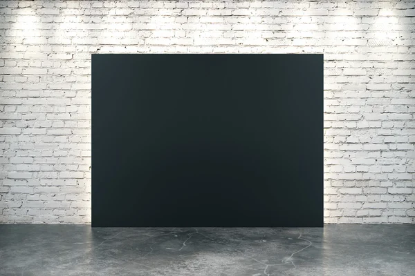 Große leere schwarze Leinwand auf Betonboden vor weißem Backsteinhintergrund — Stockfoto