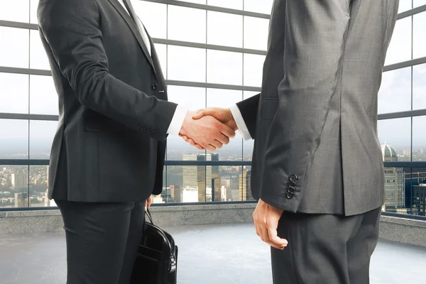 Businessmen shake hands in empty loft style room with glassy win — Stock Photo, Image