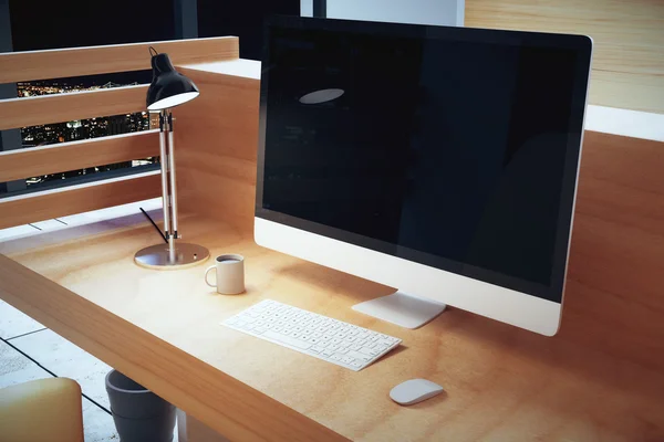 Blank black computer screen on wooden table with lamp and cup of