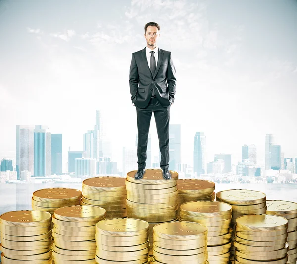 Empresário fica em pilhas de moedas conceito no fundo da cidade — Fotografia de Stock