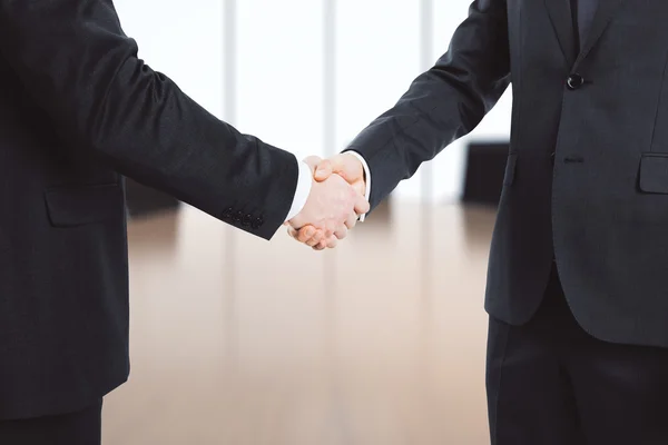 Businessmen shake hands in empty office — Stock Photo, Image