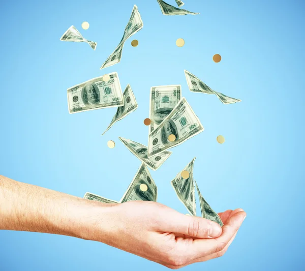 Mano humana con dinero y monedas cayendo sobre fondo azul — Foto de Stock