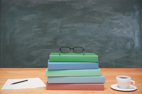 Pile of books, cup of coffee and pen on wooden table at blackboa — Stock Photo, Image