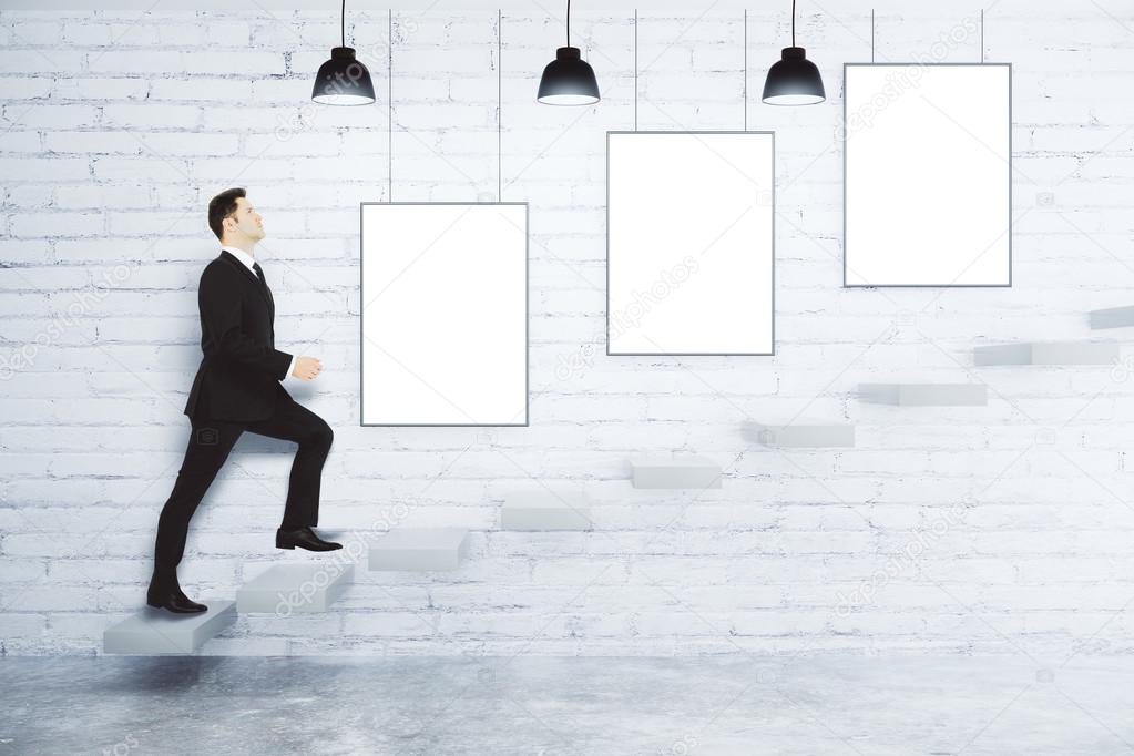 Businessman climbs up the stairs at white brick wall with blank 