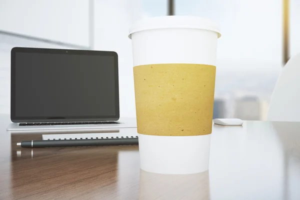 Kaffeetasse aus Papier mit Laptop und Stift auf braunem Tisch — Stockfoto