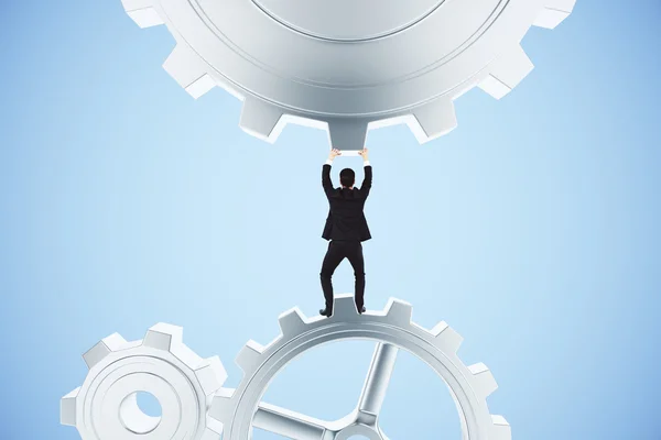 Businessman pushing gears in the mechanism on a blue background — Stock Photo, Image