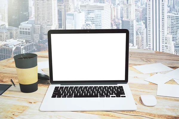 Blank laptop screen on a wooden table with cup of coffee and cit