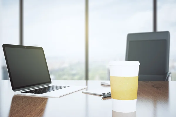 Blank coffee cup on a wooden desk and laptop, mock up