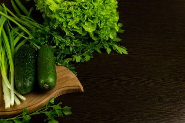 Marul yaprakları ve pırasalar kesme tahtasının üzerinde, üst manzara. Ahşap desenli arka planda marul yaprakları. Taze sebzeler. Salata hazırlığı için taze sebzeler: salatalık, salata, pırasa