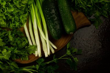 Marul yaprakları ve pırasalar kesme tahtasının üzerinde, üst manzara. Ahşap desenli arka planda marul yaprakları. Taze sebzeler. Salata hazırlığı için taze sebzeler: salatalık, salata, pırasa