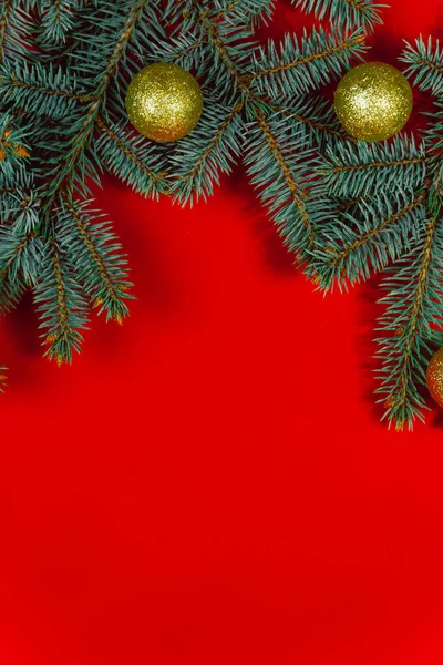 Gold-colored holiday decorations are beautifully laid out on pine branches against a red background. Christmas background. Holiday decorations on a Christmas background. Christmas composition with dec