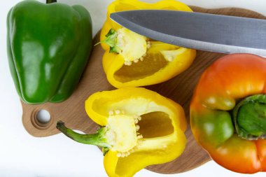 Yeşil saplı, kırmızı, yeşil ve sarı biberli taze sebzeler ve soyutlanmış beyaz arka planda bir kesme tahtasının üzerinde duran bir bıçak. Yukarıdan bak. Taze sebze..