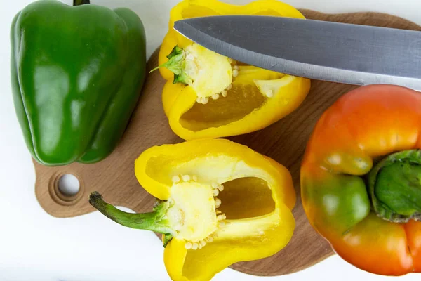 Yeşil saplı, kırmızı, yeşil ve sarı biberli taze sebzeler ve soyutlanmış beyaz arka planda bir kesme tahtasının üzerinde duran bir bıçak. Yukarıdan bak. Taze sebze..
