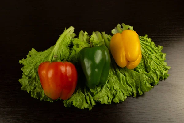 Fresh vegetables, red, yellow, green peppers lie on lettuce leaves on a dark wooden background. View from above.