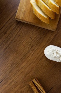 Tahta bir kaşıkta un, tahta bir tahtanın üzerinde dilimlenmiş Fransız ekmeği ve ahşap bir masada tarçın çubukları. Kopyalama alanı olan üst görünüm. Metin veya logo için yeri olan mutfak pişirme araçları.