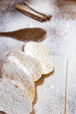 Tahta bir tahtanın üzerinde dilimlenmiş Fransız ekmeği, tarçın çubukları ve ahşap bir masanın üzerinde ağır şekilde un kaplı büyük bir kaşık izi..  