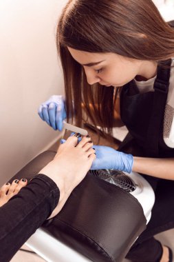 Mavi eldivenli kız pedikür yapıyor. Kuaförde kadın donanım pedikürü var. Profesyonel pedikür. Tırnaklarını temizle..