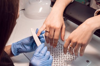 Manikür ustası müşteri için mavi eldivenli manikür yapıyor. Güzellik salonunda erkek manikürü. Erkek manikürü. Usta, elinde tırnak törpüsü olan bir adamın tırnaklarını testereyle keser.