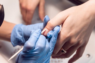 Bir manikürcü müşterisi için mavi eldivenli manikür yapar. Güzellik salonunda erkek manikürü. Turuncu çubuk, tırnak etleriyle çalışıyor. Tırnağı turuncu bir çubukla geriye it. Erkek manikürü..