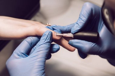 Bir manikürcü, jöle oje kullanan bir müşteri için mavi eldivenli manikür yapar. Kuaförde kadın manikürü. Bir manikürcü güzellik salonunda oje sürüyor. Manikürcü.