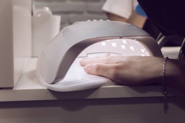 Kız jöle sürdükten sonra tırnaklarını lambayla kurutuyor. Bir kadının eli, tırnaklarını ultraviyole lambayla kurutur. Manikür. Güzellik salonu..