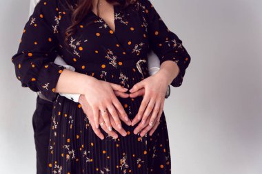 Aşk ve ilişkiler beyaz bir arkaplanda. Çocuk beklentisi içinde bir aile, hamile bir kızın karnında bir kalp. Adam hamile kızı karnından tutuyor..