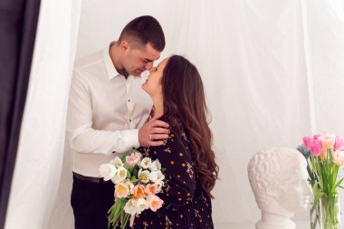 Aşk ve ilişkiler. Beyaz havadar kumaşlı arka planda mutlu bir çift. Beyaz arka planda bir buket lale ve mesaj için yeri olan bir kız..