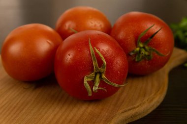 Yeşil kuyruklu kırmızı domatesler ahşap bir tahtada ve koyu dokulu ahşap arka planda yatar. Bitkilerle. Çevre dostu domatesler. Taze domates. Su damlalı domatesler. taze sebze