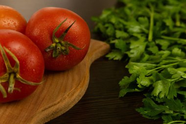 Yeşil kuyruklu kırmızı domatesler ahşap bir tahtada ve koyu dokulu ahşap arka planda yatar. Bitkilerle. Çevre dostu domatesler. Taze domates. Su damlalı domatesler. taze sebze