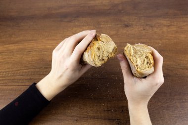 Kız, tahta bir arka planda iki eliyle bir baget tutuyor. Siyah kollu kadın elleri, koyu dokulu ahşap bir masada gevrek beyaz bir baget tutuyor. Yukarıdan görüntüle.